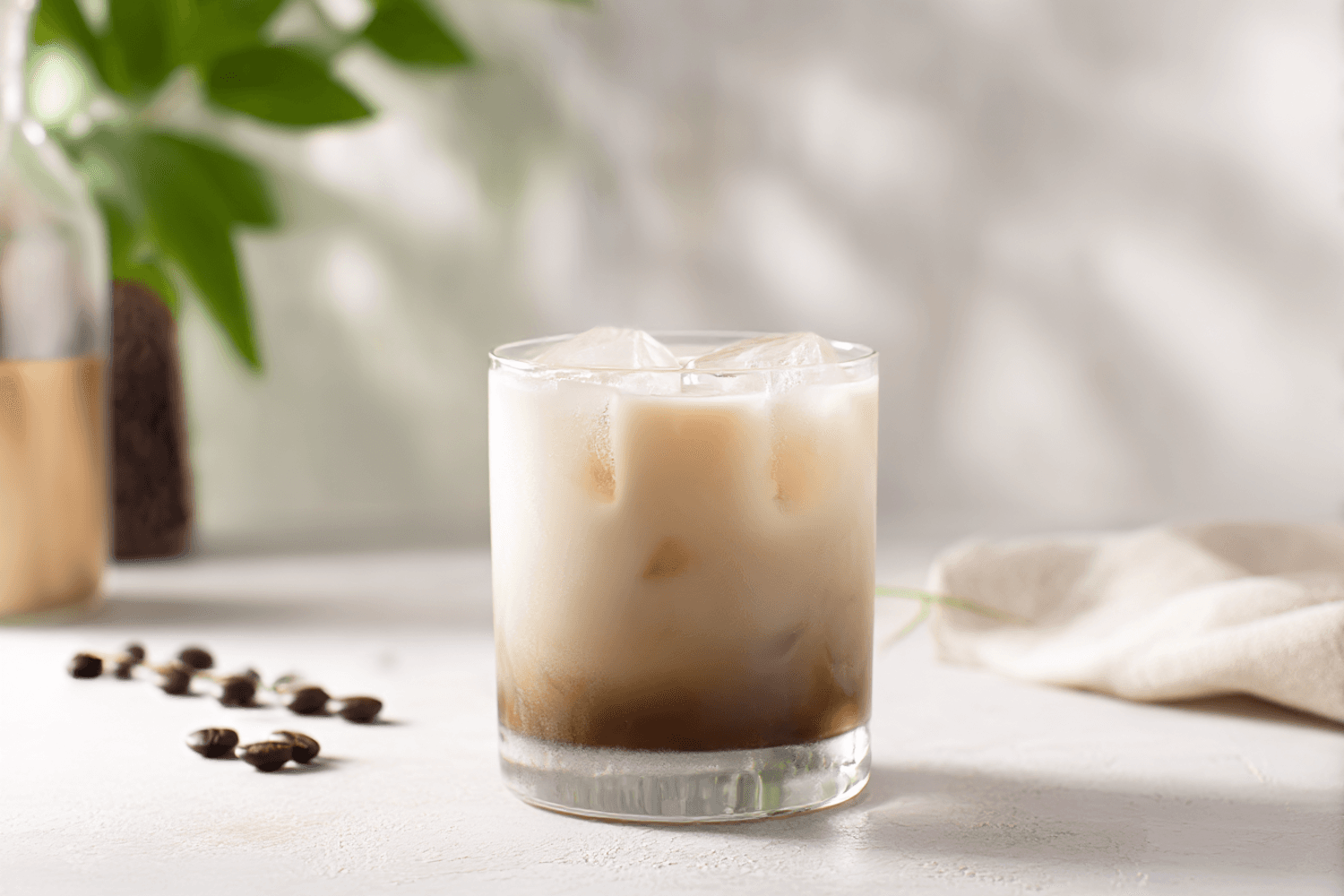 An iced latte in a short glass with coffee beans scattered beside it