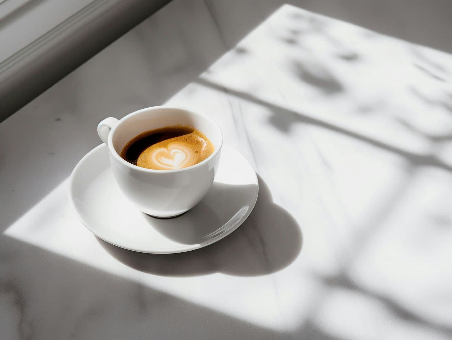 A cup of coffee with heart latte art on a sunlit window table